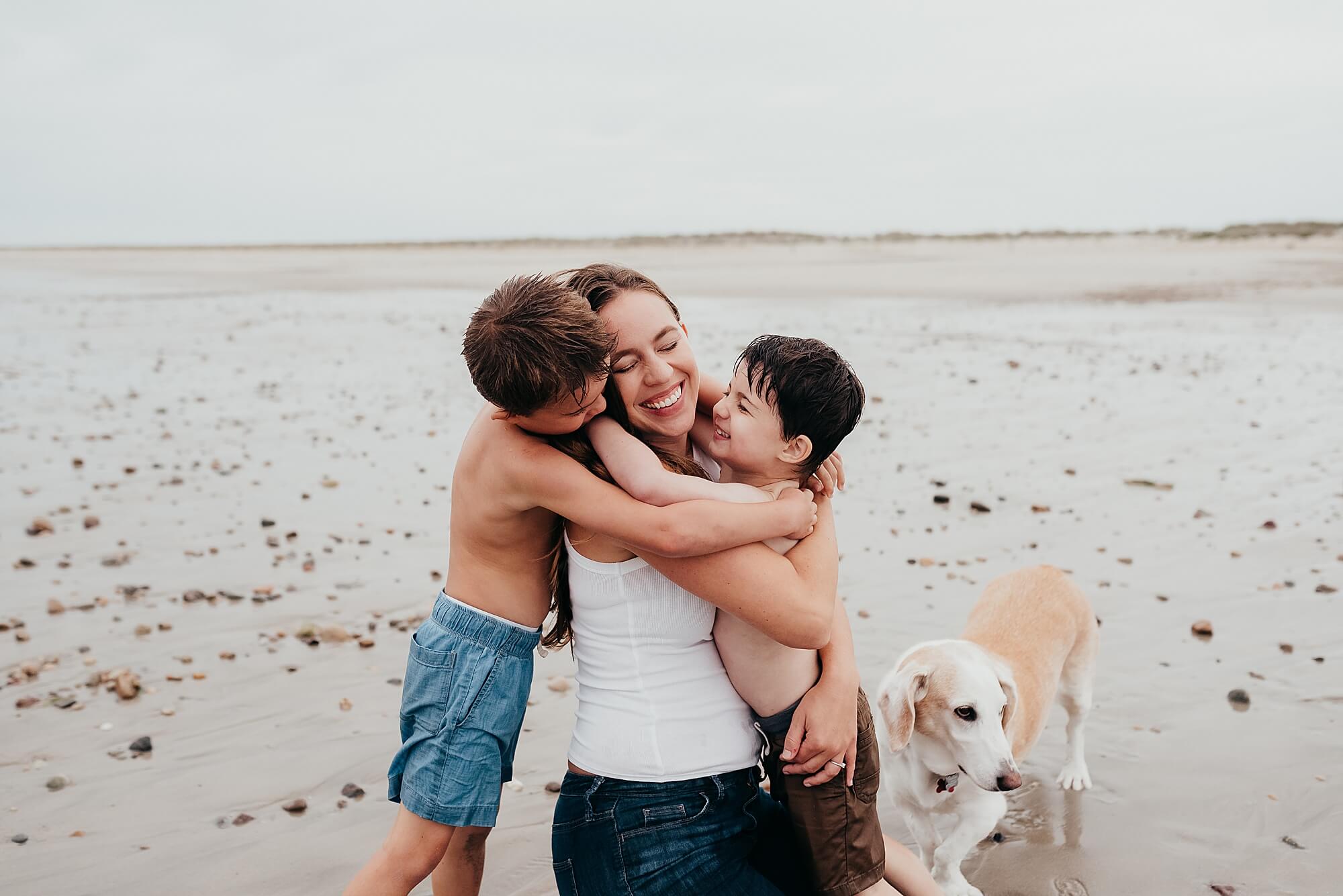 An image of a mother and her young boys in a joyful hug on the beach during their cape cod family photographer session