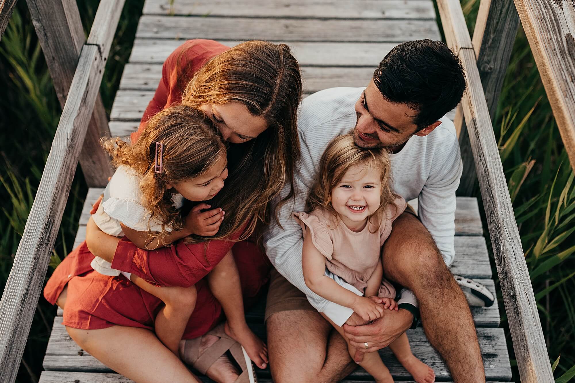 a family snuggles together on a boardwalk, they are all laughing and smiling during their cape cod family photographer session