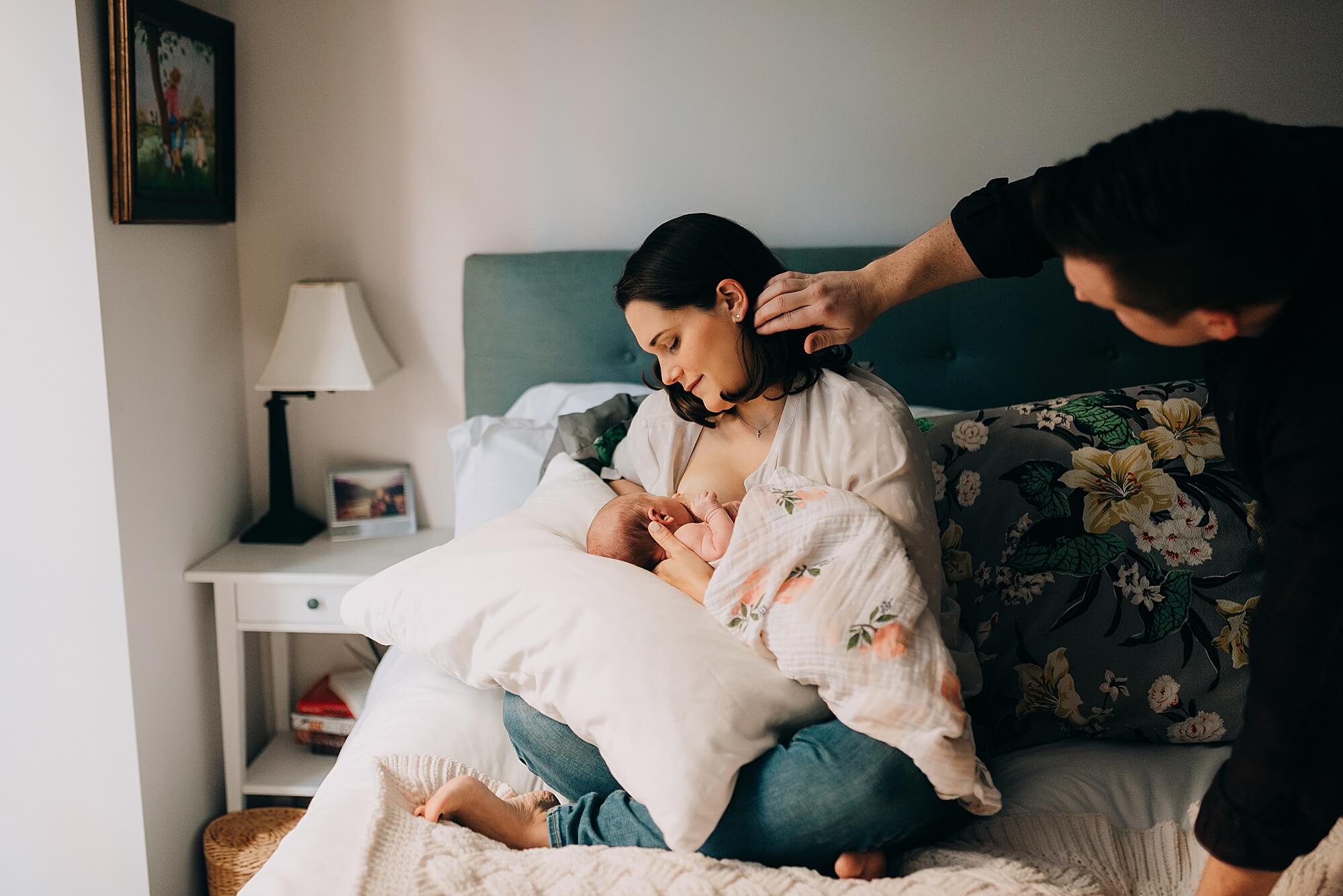 a mother nurses her newborn daughter while her husband brushes her hair away from her face during their cape cod family photographer session