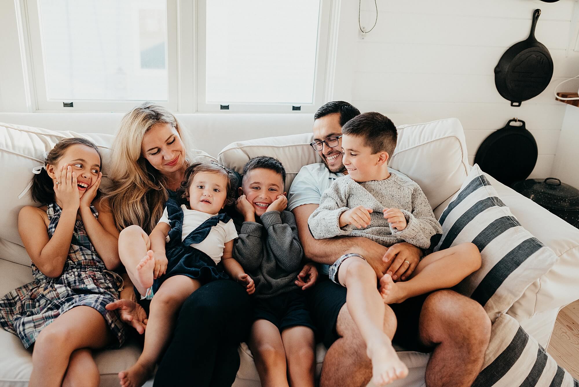 A family snuggles and laughs together on a couch in a bright white living room