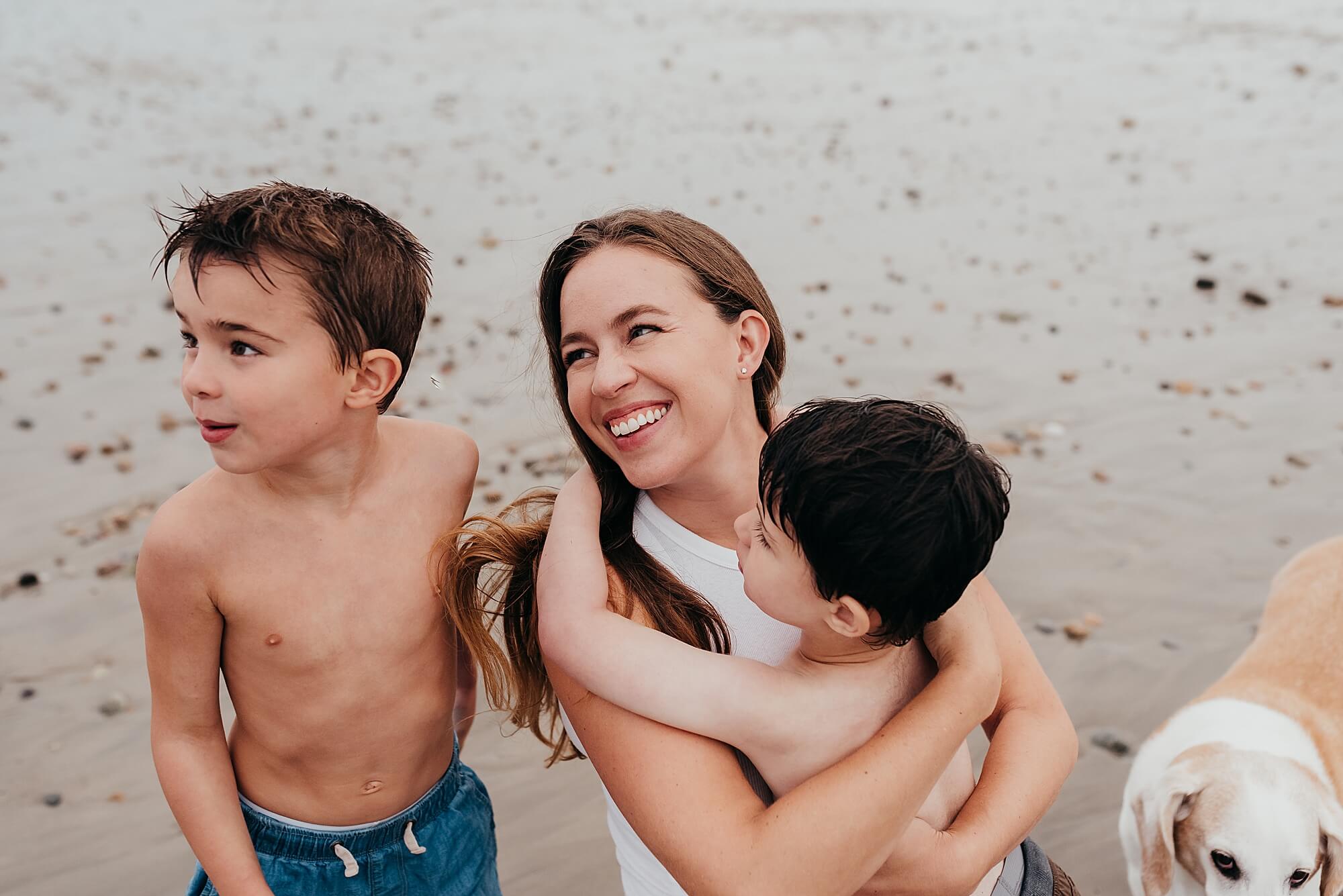 A mother hugs her son on the beach while she looks up at her husband who is off camera