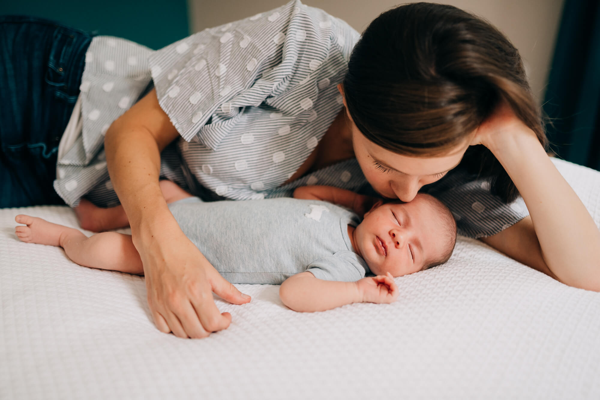 a mother gently leans over to kiss her newborn son during their newborn photography south shore ma photoshoot