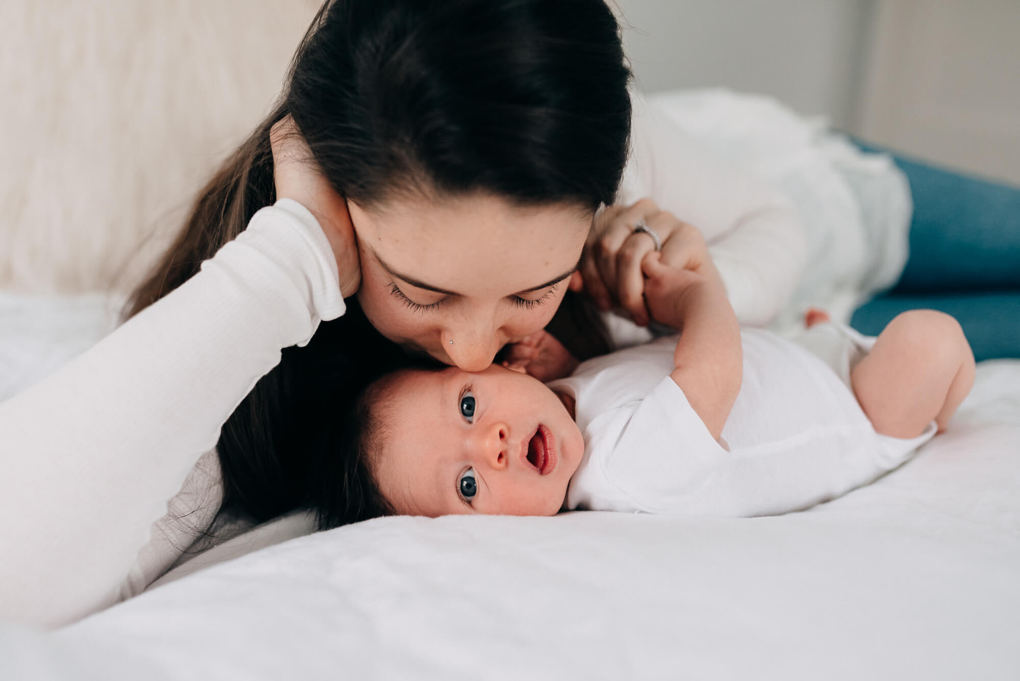 a mother gently kisses her newborn son as they snuggle in bed during their newborn photography south shore ma photoshoot