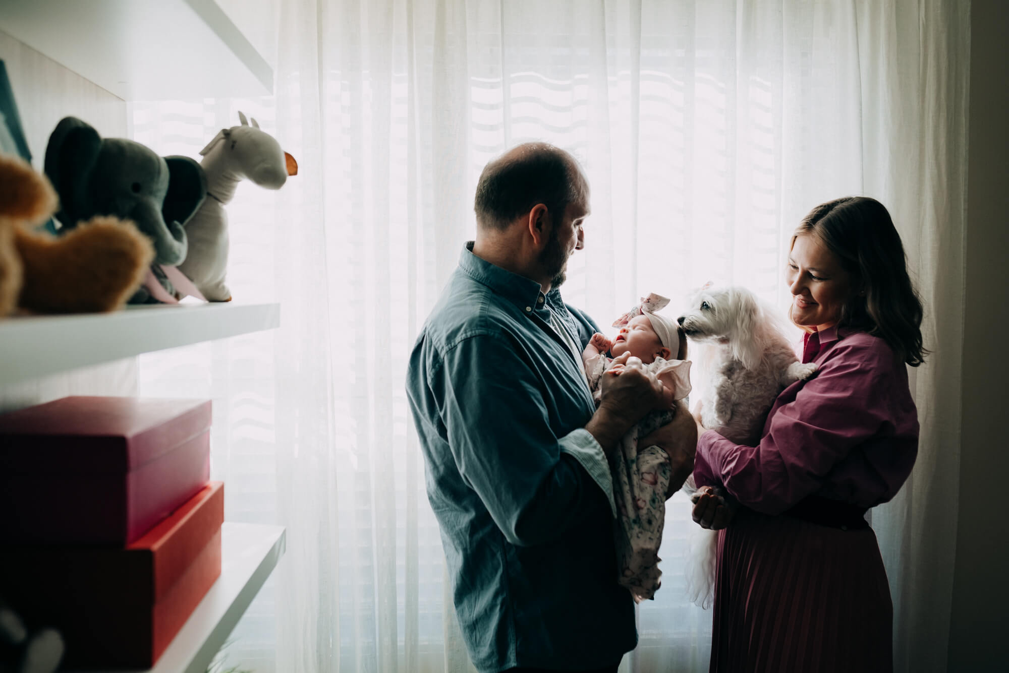 parents hold their newborn daughter next to a bright window