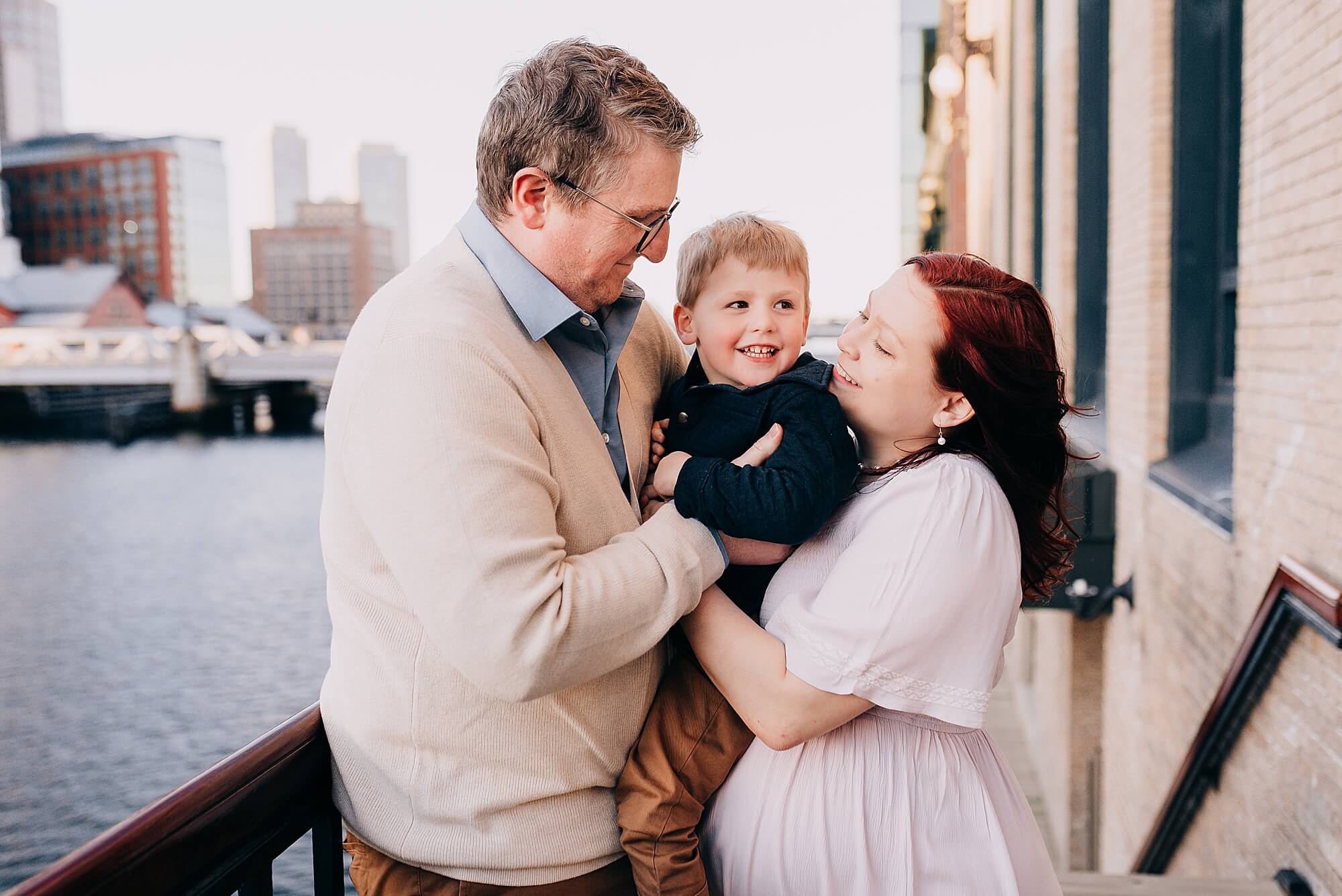 A mother and father hold their young son and smile at him at the seaport in Boston