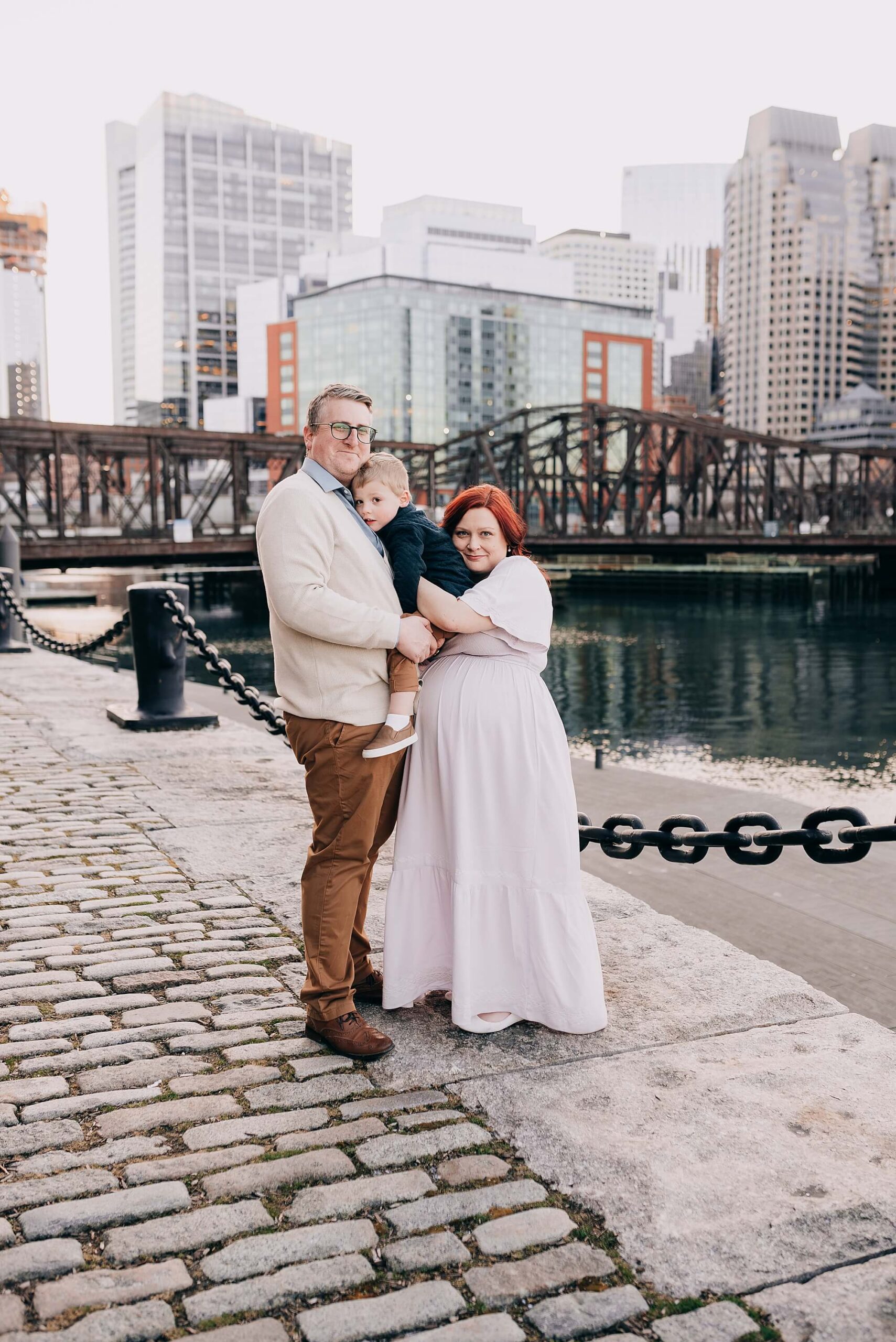 A mother and father snuggle their son at sunset at the seaport Boston