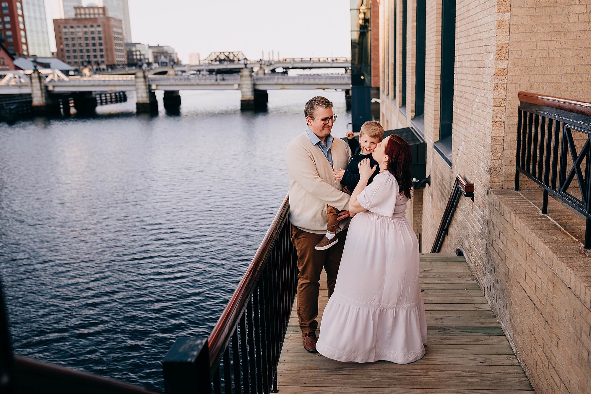 A mother and father snuggle their son next to the water at the seaport Boston