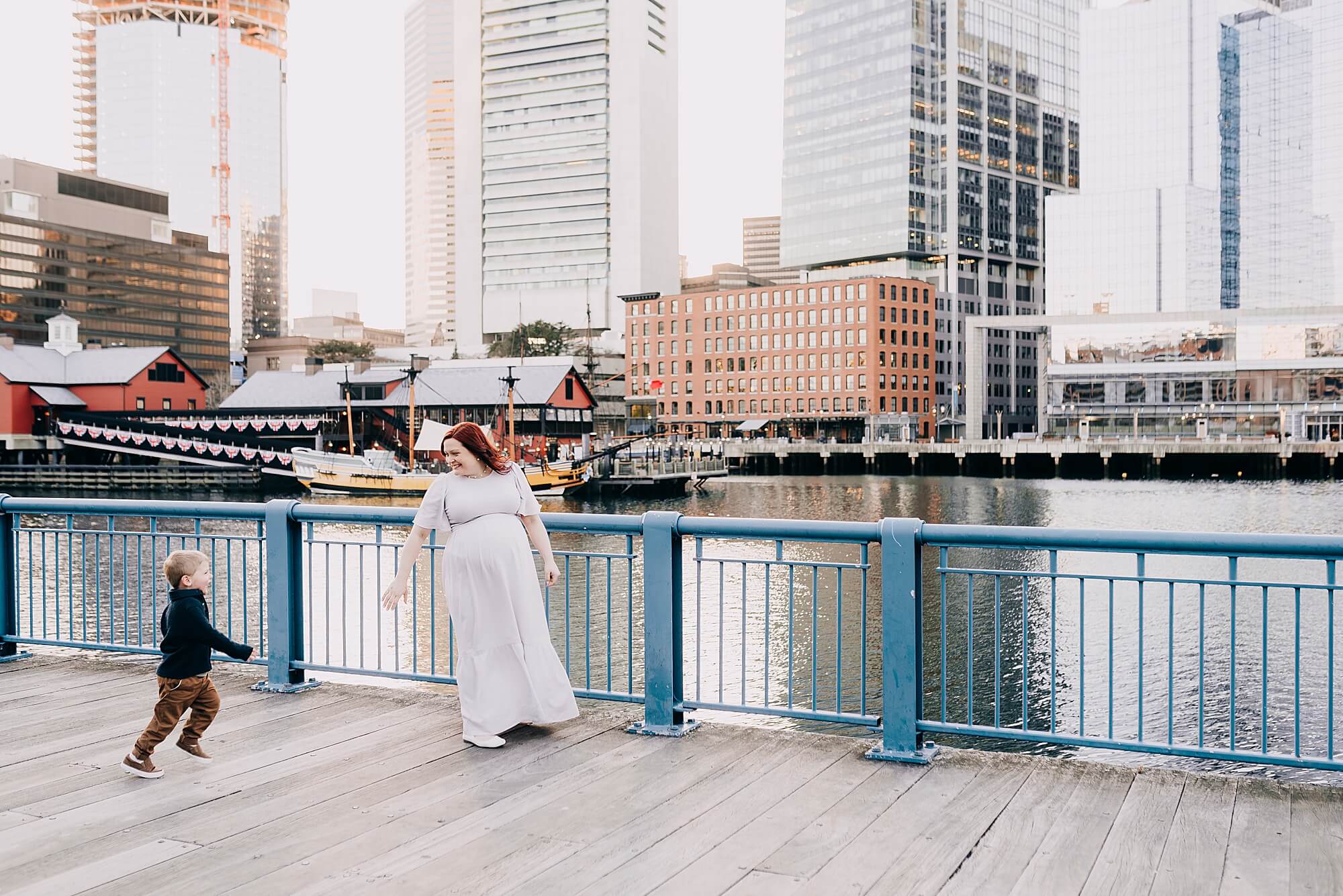 An expecting mother reaches for her young son's hand at the seaport during their Boston Maternity Photographer session