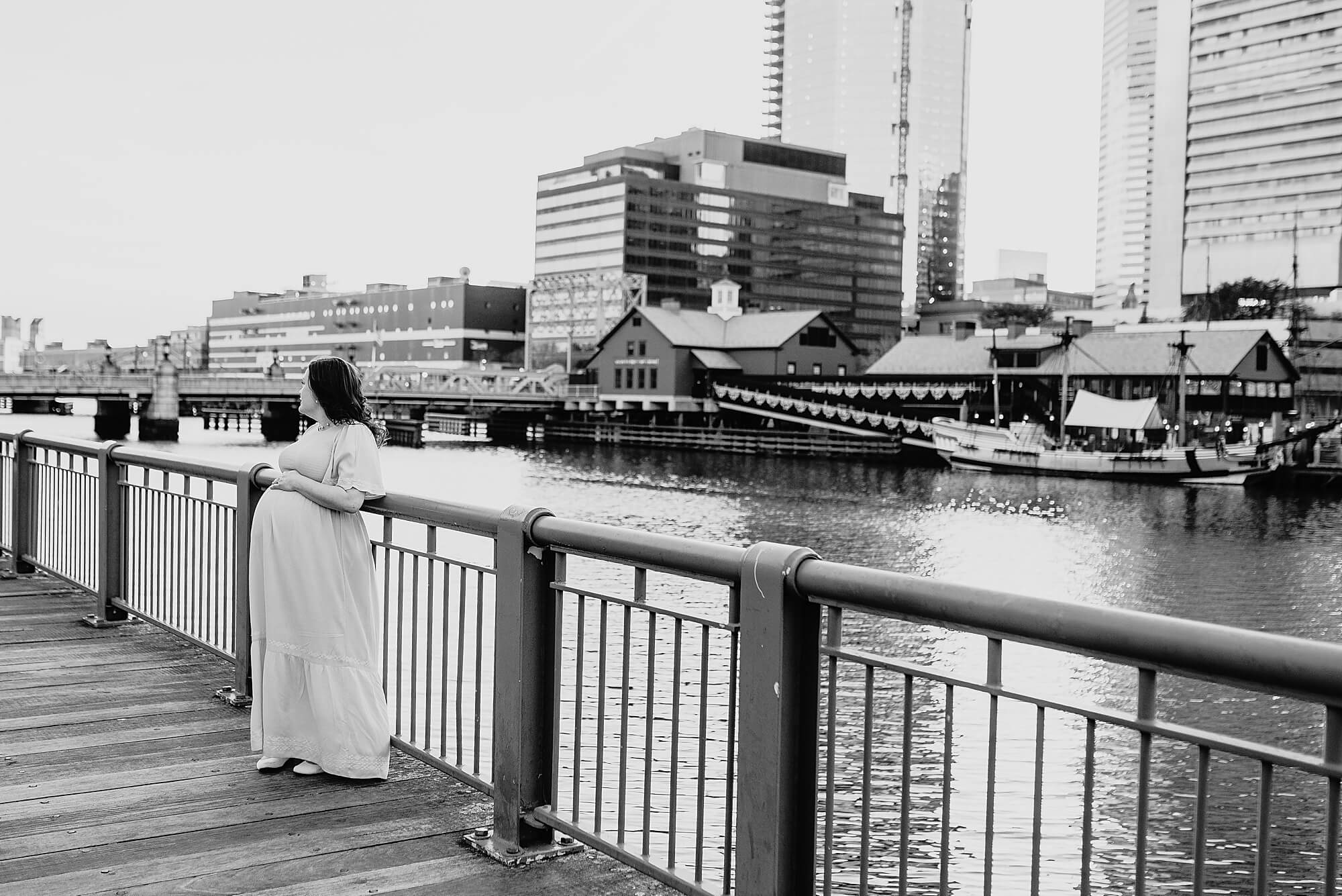 A pregnant mother leans against the railing in front of a boat during her Boston Maternity Photographer session