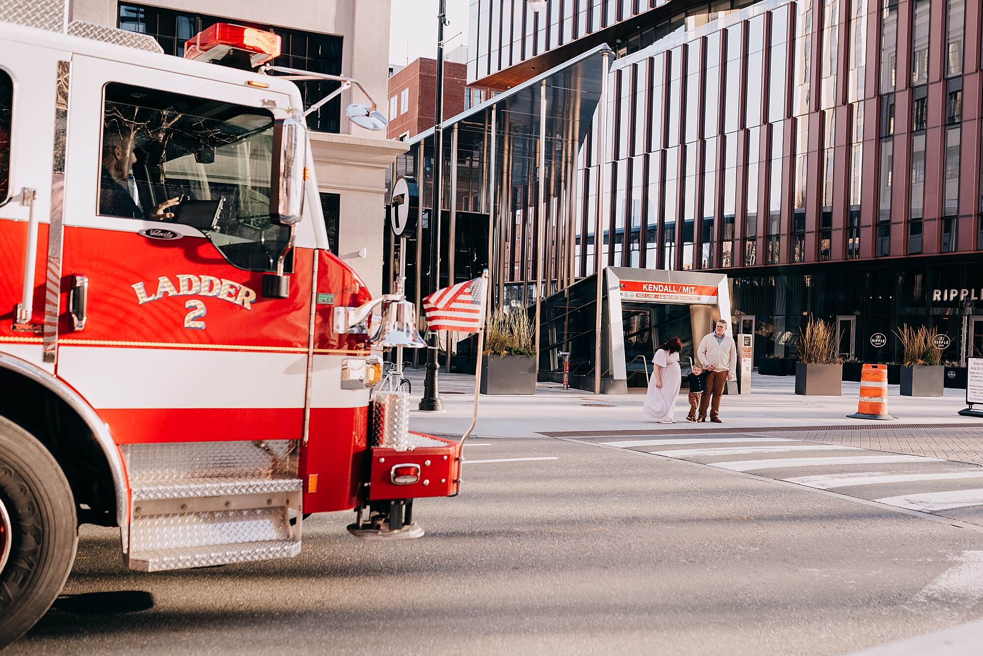 a family stands in front of Kendall station in Boston, a fire truck passes by in the foreground