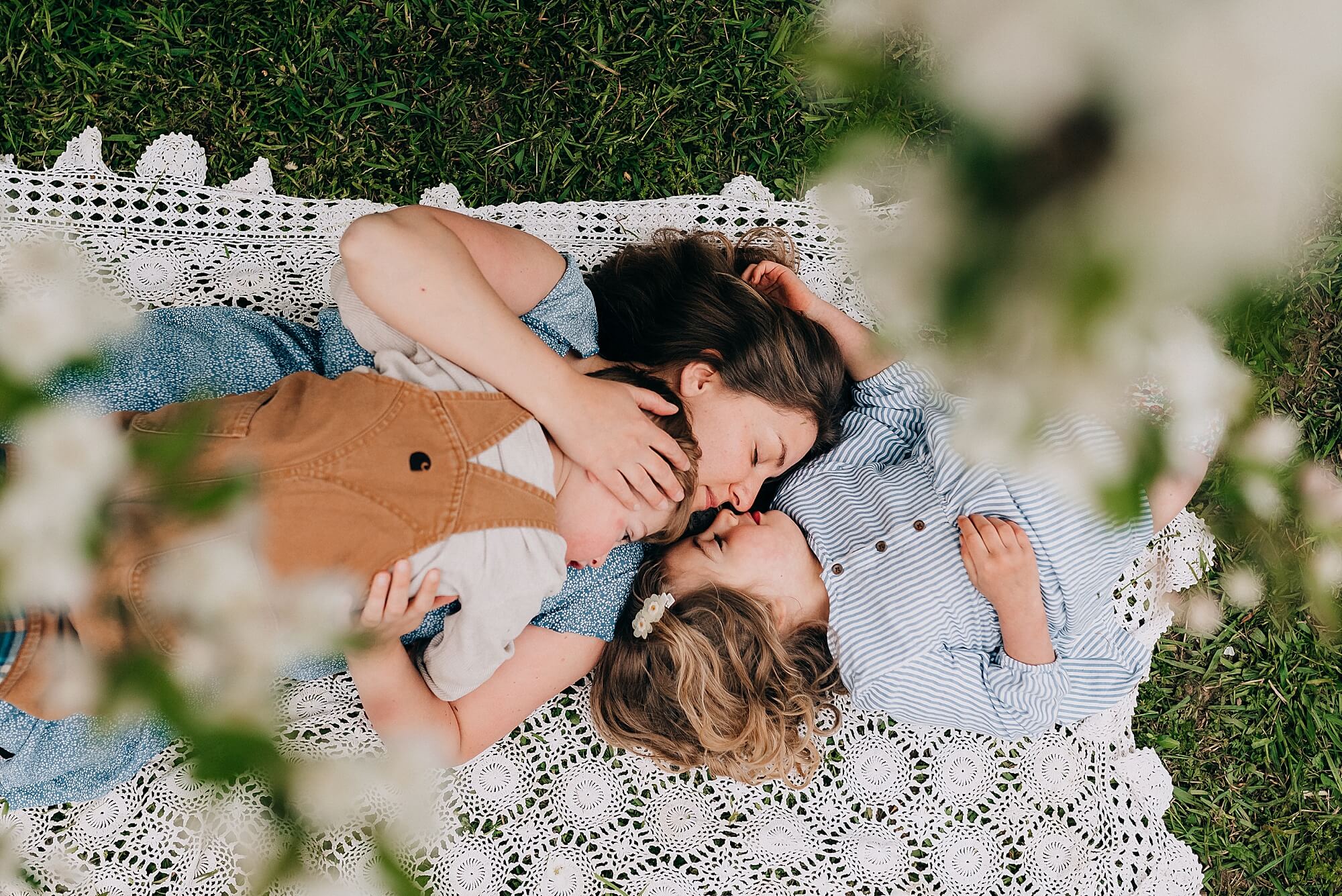 A mother lays on a blanket with her two children under a blossoming tree