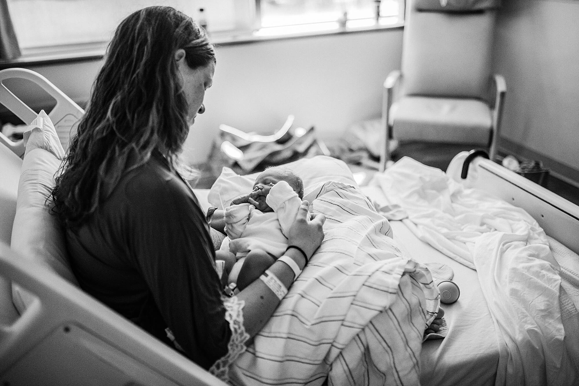 A mother looks on at her brand new baby in her hospital room after giving birth