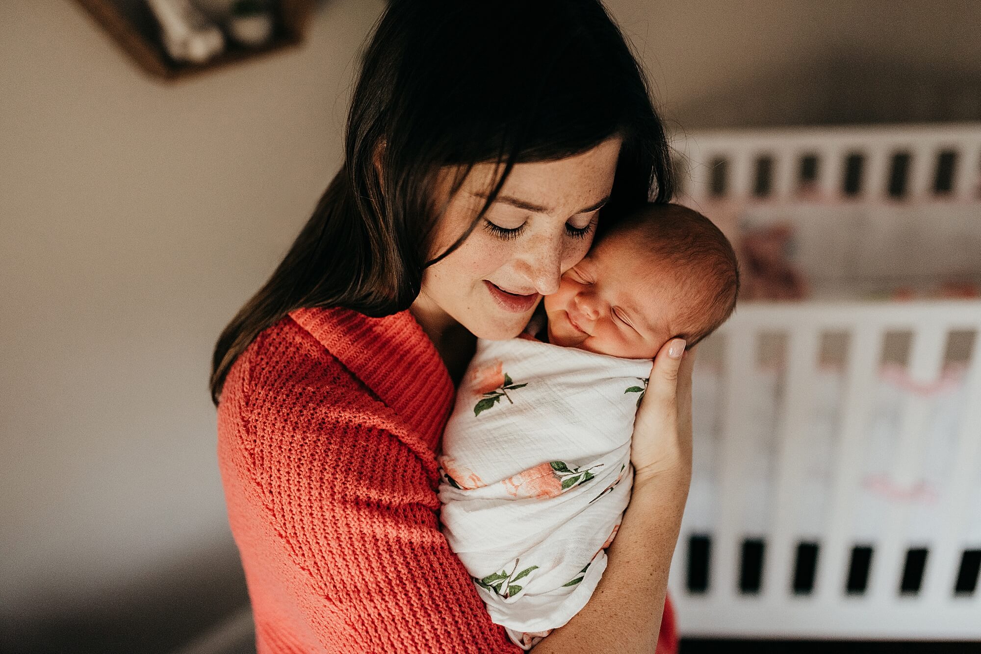 A mother snuggles her newborn daughter next to her face in her nursery