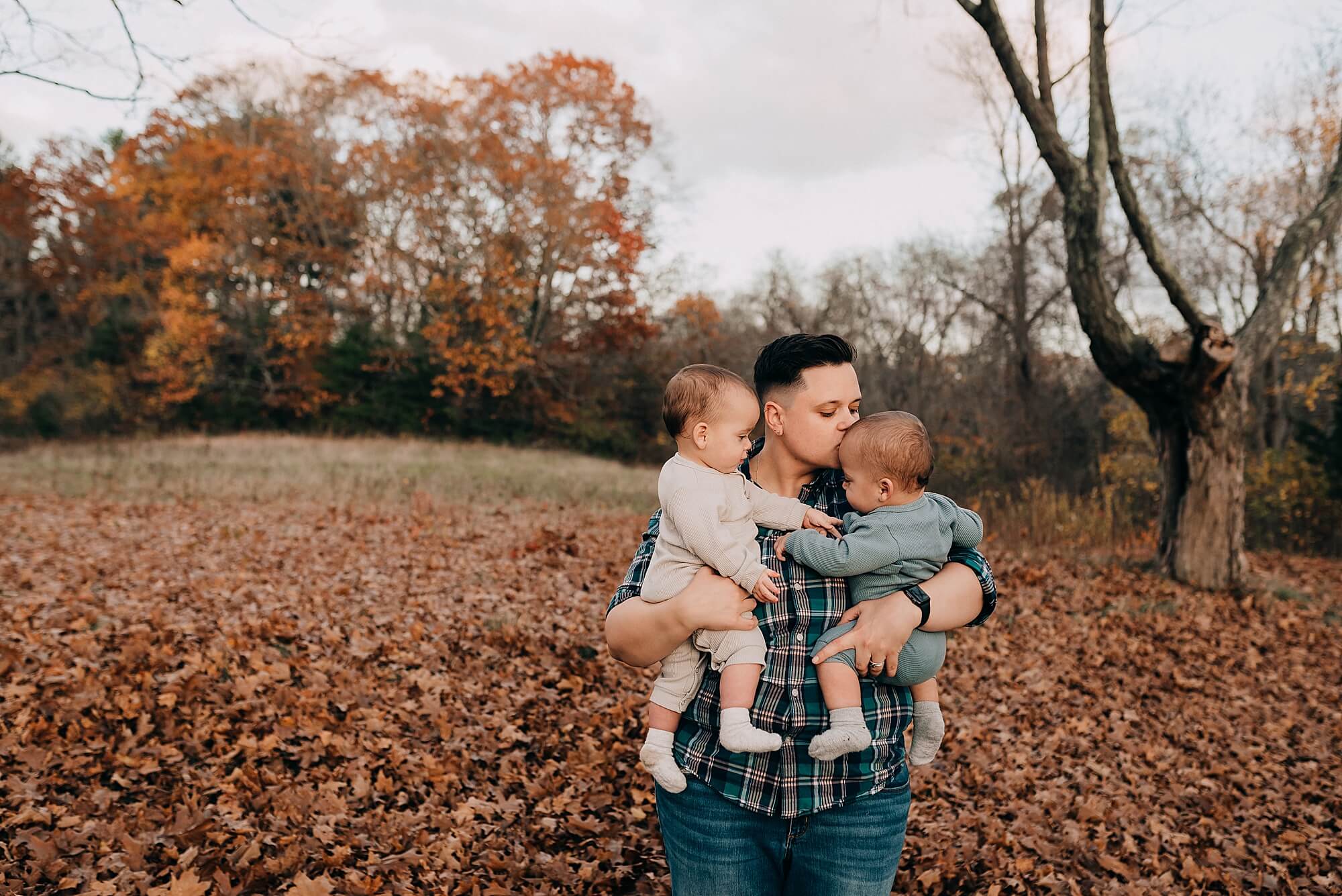 A mother holds her twin babies near autumn leaves