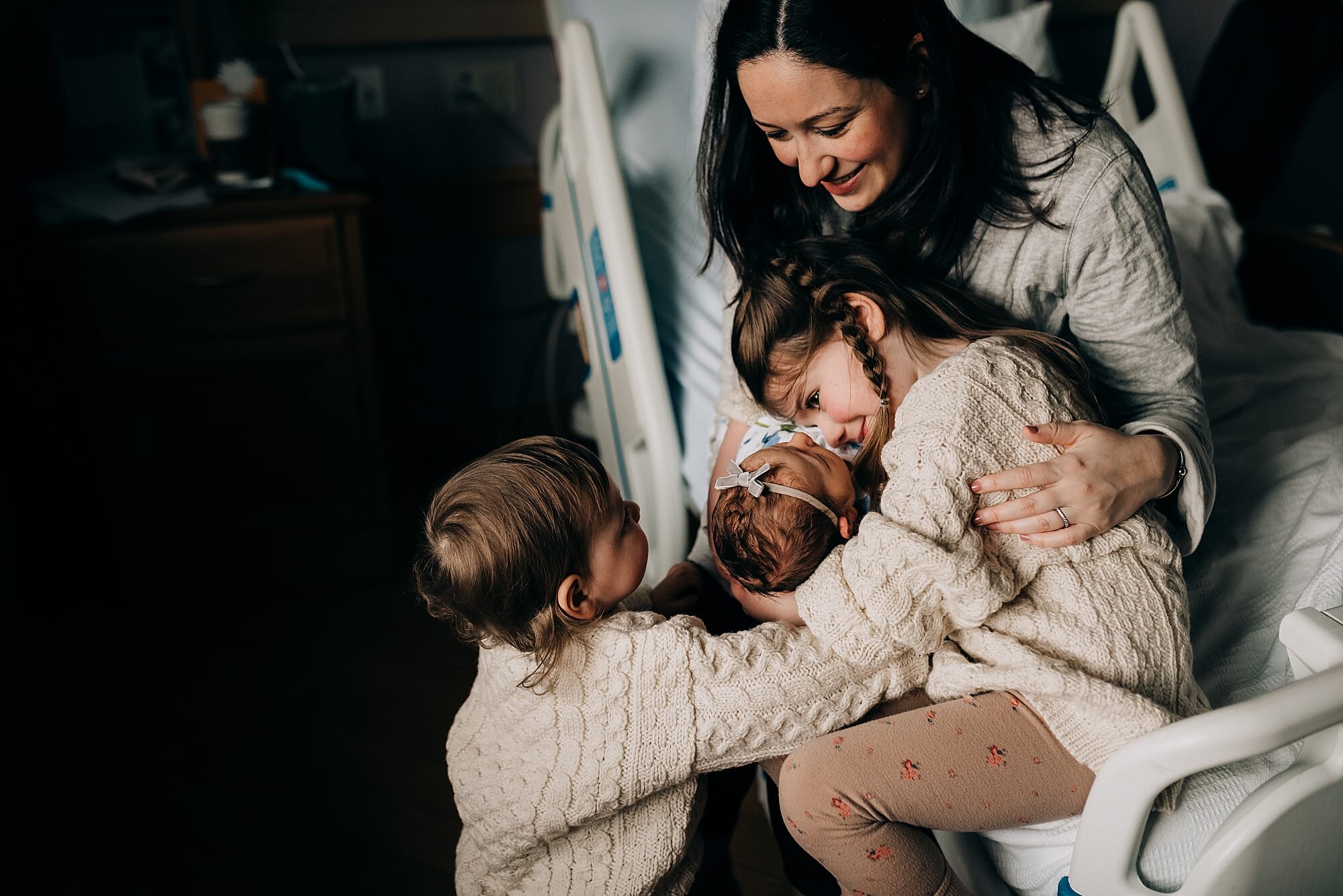 A mother introduces their new sibling to her older children in the hospital after she's given birth