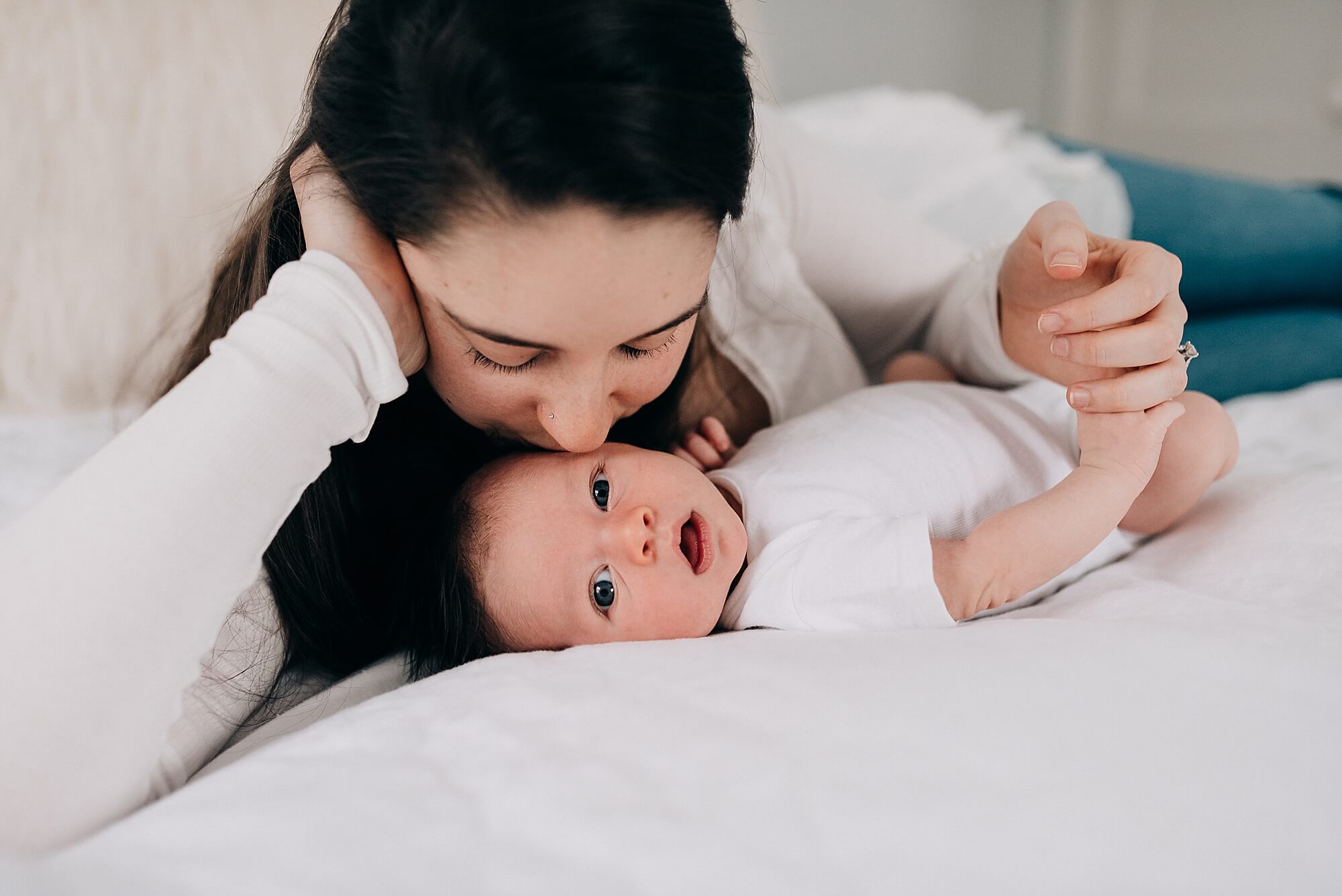 A Hingham mother lays on the bed next to her baby, giving him a kiss on the cheek