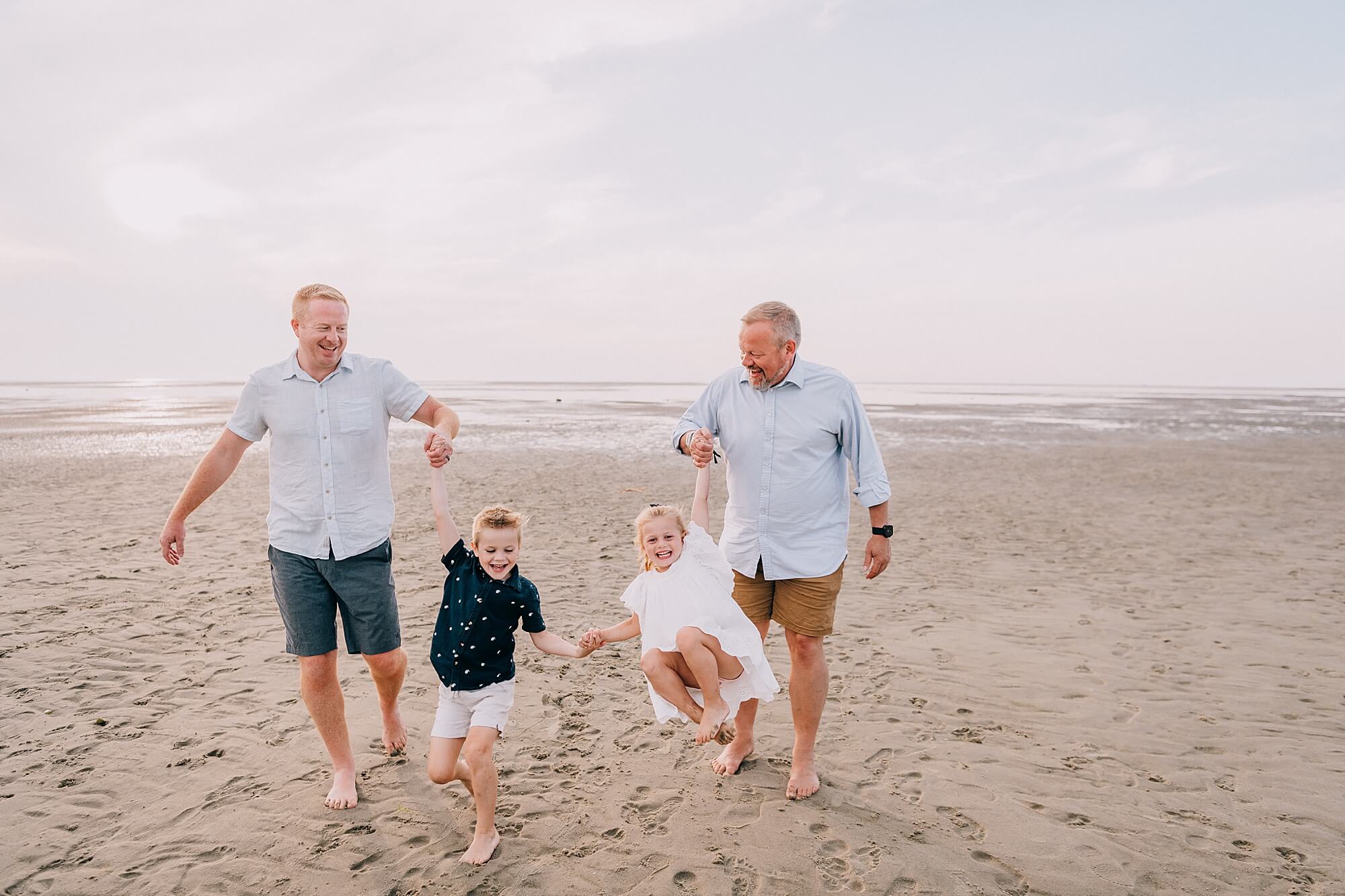 Two dads swing their kids at the beach on Cape Cod with Cape Cod Family Photographer, Allison Wolf