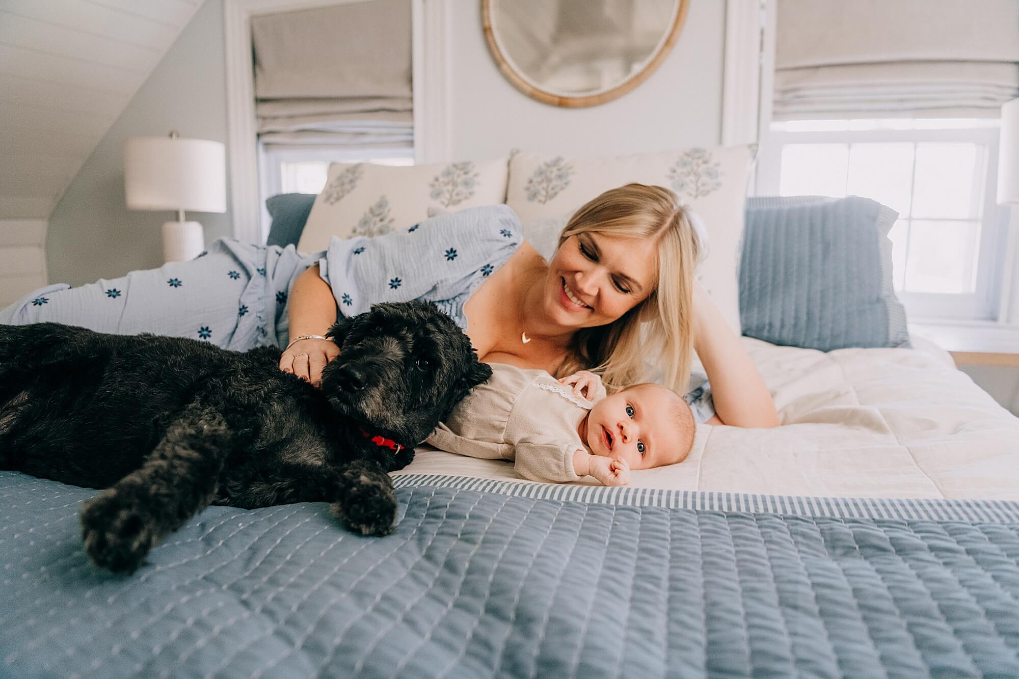A mother rests on the bed with her newborn baby girl and dog